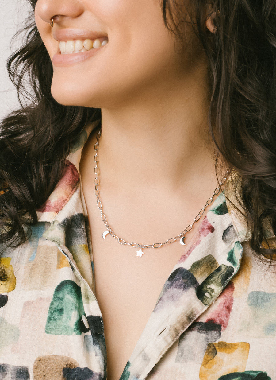 Charm necklace from RIVA New York featuring star and moon charms dangling from a rounded paper clip chain, seen here in sterling silver