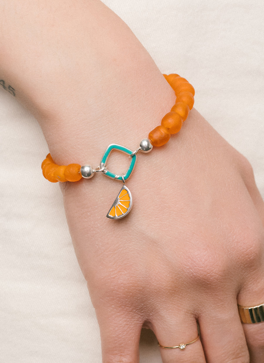 Citrus wedge charm from RIVA New York jewelry, featuring orange enamel on sterling silver; shown here worn with cushion Invisible Clasp and Sunset recycled glass bead bracelet