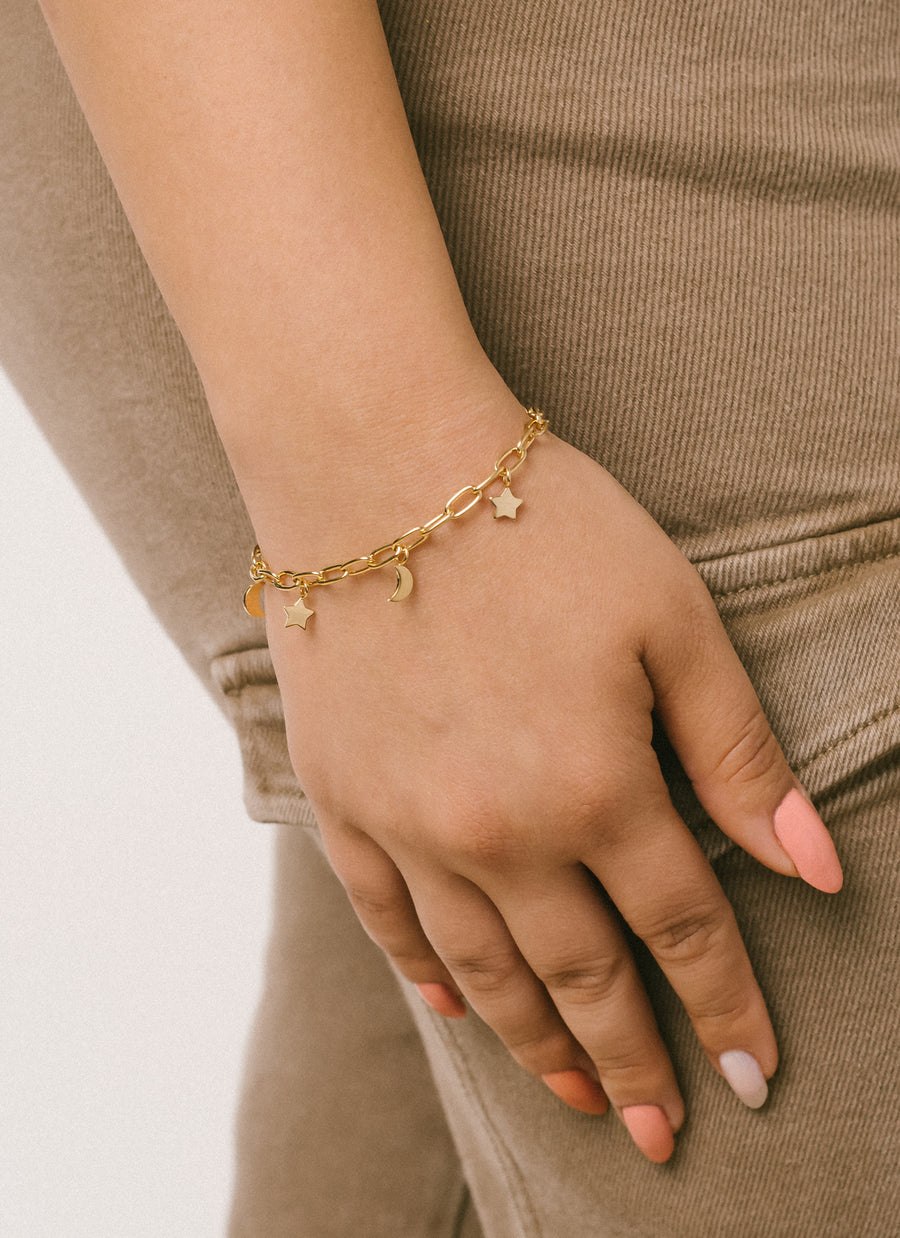 Hand model wearing charm bracelet from RIVA New York featuring moon and star charms dangling from a rounded wire paper clip chain